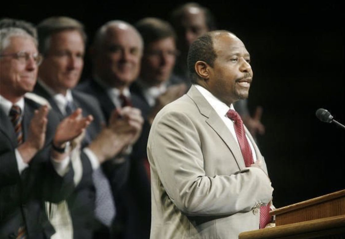 Paul Rusesabagina speaking in a tan suit with a red tie, photo taken before his kidnapping by the Rwandan government.