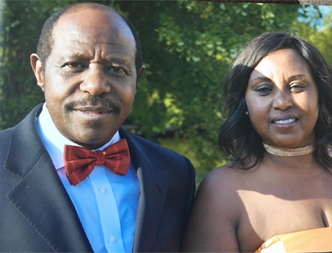 Paul Rusesabagina, humanitarian and political prisoner wears a black suit and red bow tie in a photo with his wife. They are smiling and looking at the camera.