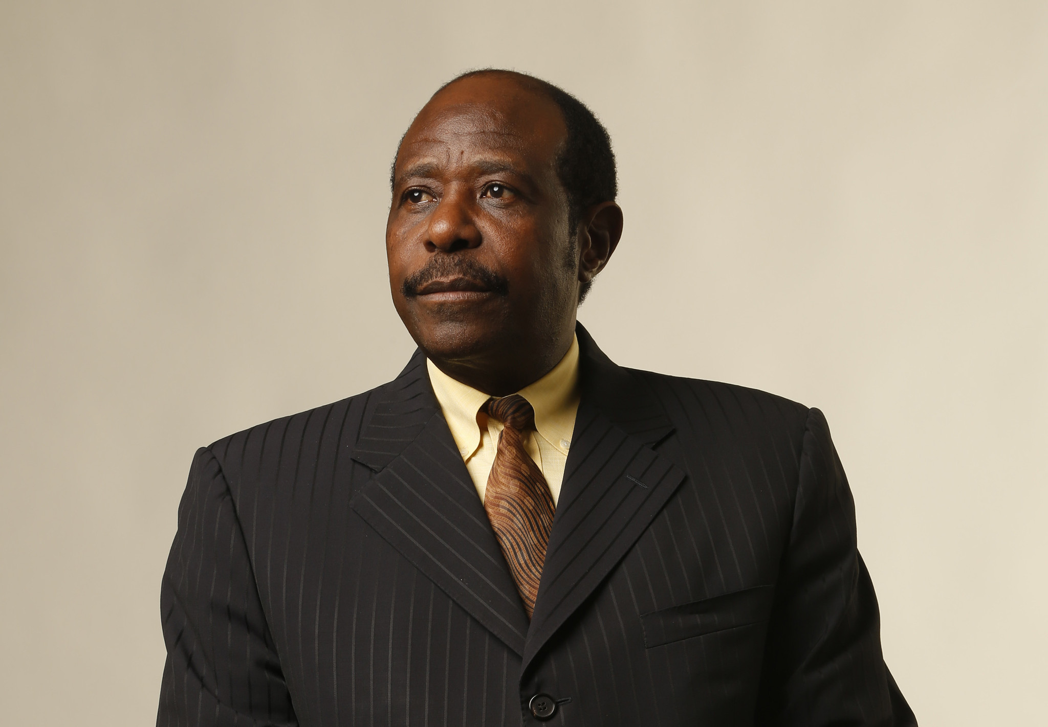 Paul Rusesabagina, humanitarian and political prisoner wears a black suit and brown tie, he looks away from the camera.